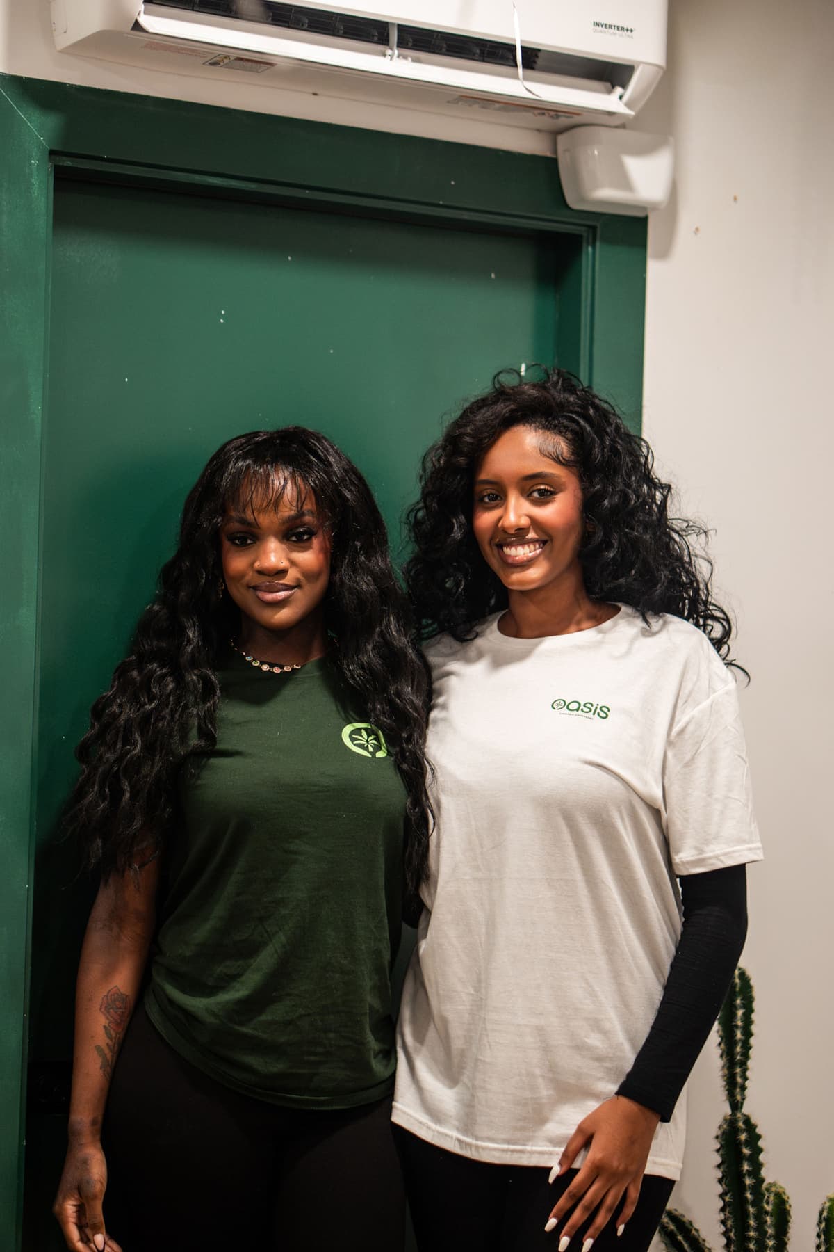 Two Oasis team members smiling together in front of the shop's green door